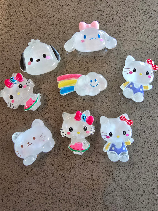 Set de 8 charms kawaii translúcidos dispuestos sobre superficie beige: Cinnamoroll con moño rosa, perrito blanco con orejas negras, Hello Kitty con moño a cuadros, nube sonriente con arcoíris multicolor, Hello Kitty con vestido morado, osito blanco translúcido, Hello Kitty con moño rosa y sandía, Hello Kitty con vestido azul, todos con acabado cristalino y detalles coloridos 