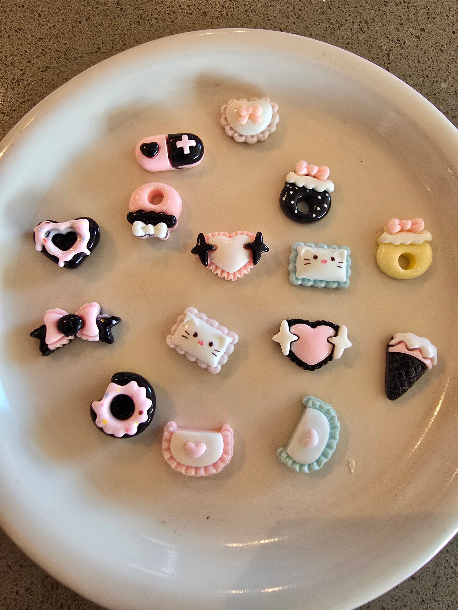 Variedad de figuritas kawaii pequeñas en rosa y negro sobre plato blanco"