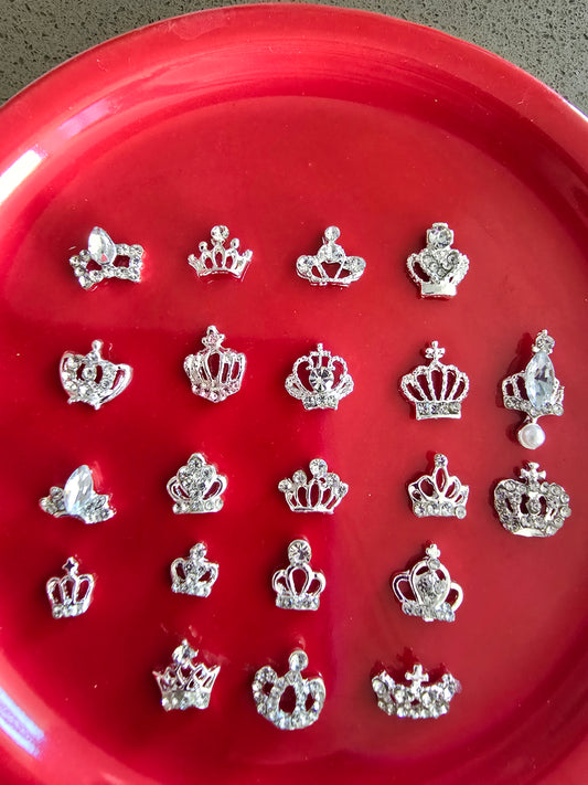 Set de 10 mini coronas plateadas con cristales brillantes organizadas en bandeja roja, mostrando diferentes diseños de tiaras reales con acabados metálicos, perfectas para nail art y decoración premium 