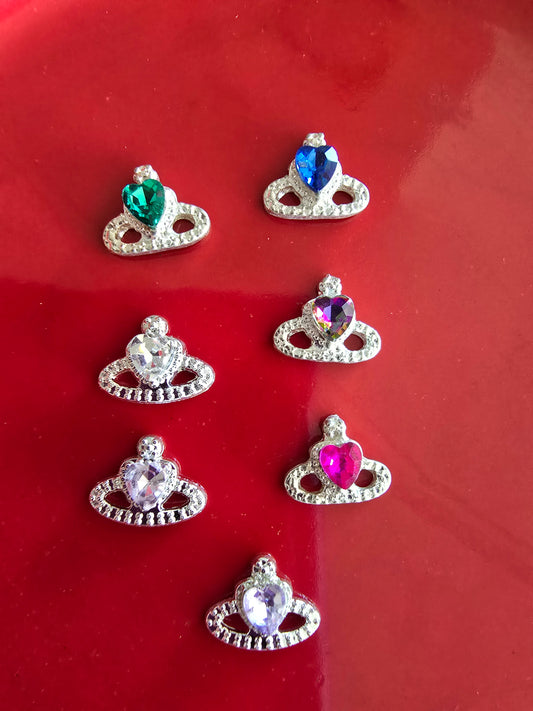 Set de 10 coronas reales decorativas para nail art con gemas multicolor sobre fondo rojo, mostrando coronas doradas con gemas centrales en verde, azul, multicolor, cristal transparente, púrpura y rosa, cada una rodeada de cristales brillantes

