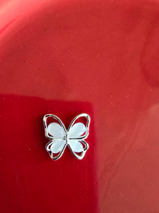 Mariposa plateada decorativa para nail art sobre fondo rojo, mostrando acabado metálico brillante con detalles delicados, ideal para decoración de uñas y manicure profesional

