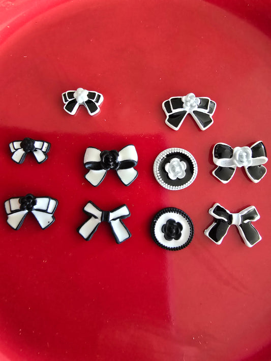 Set de 10 lazos decorativos para nail art en blanco y negro sobre fondo rojo, mostrando diferentes diseños incluyendo lazos simples, lazos con flores centrales y detalles decorativos variados

